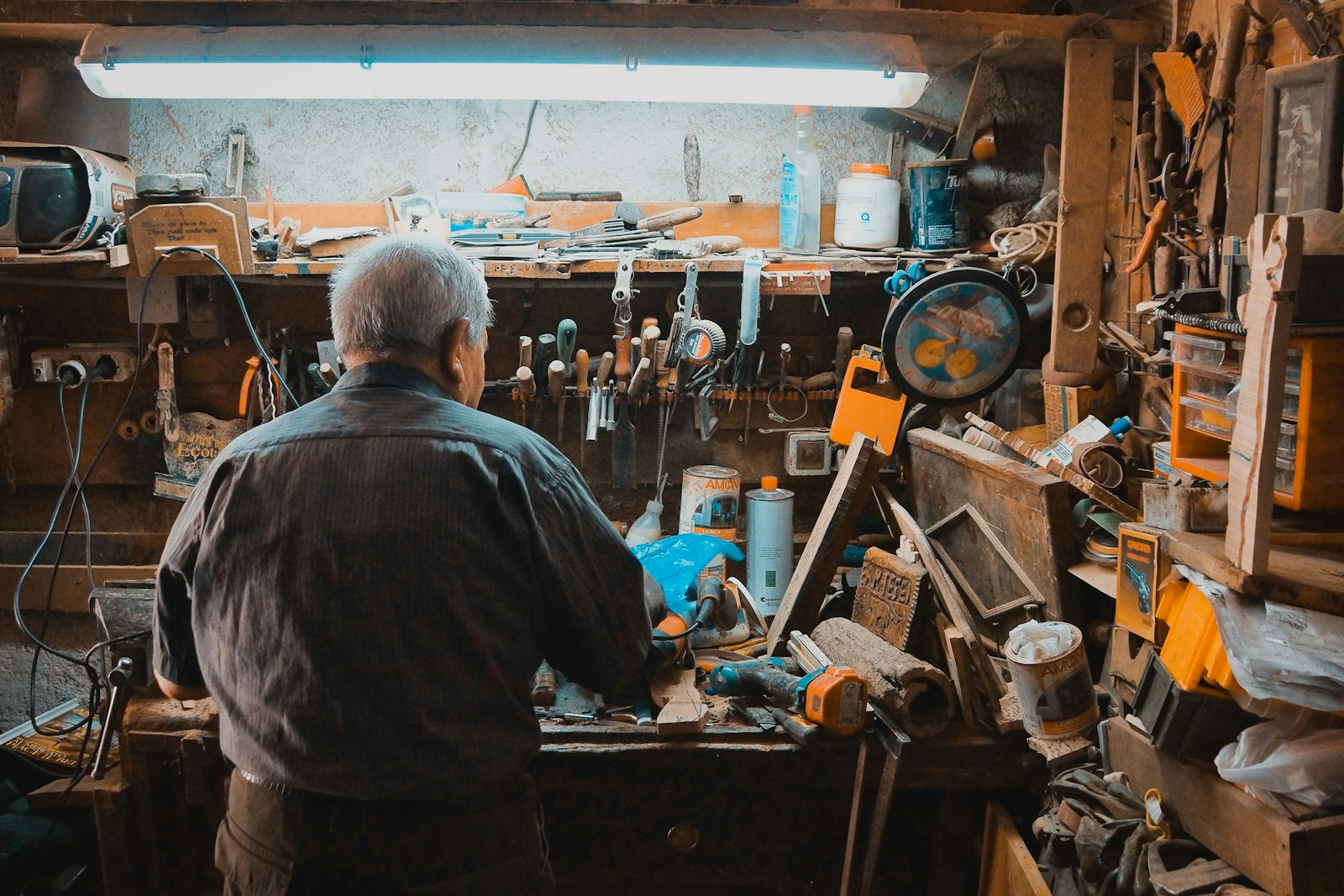 Artisan de dos devant son établi, outils accrochés au mur